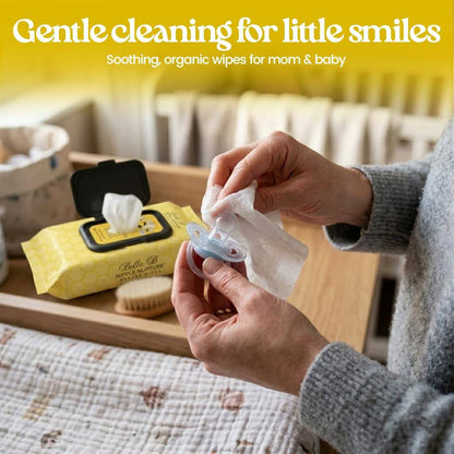 Person using organic wipes to clean a baby pacifier with text 'Gentle cleaning for little smiles' on a yellow background.